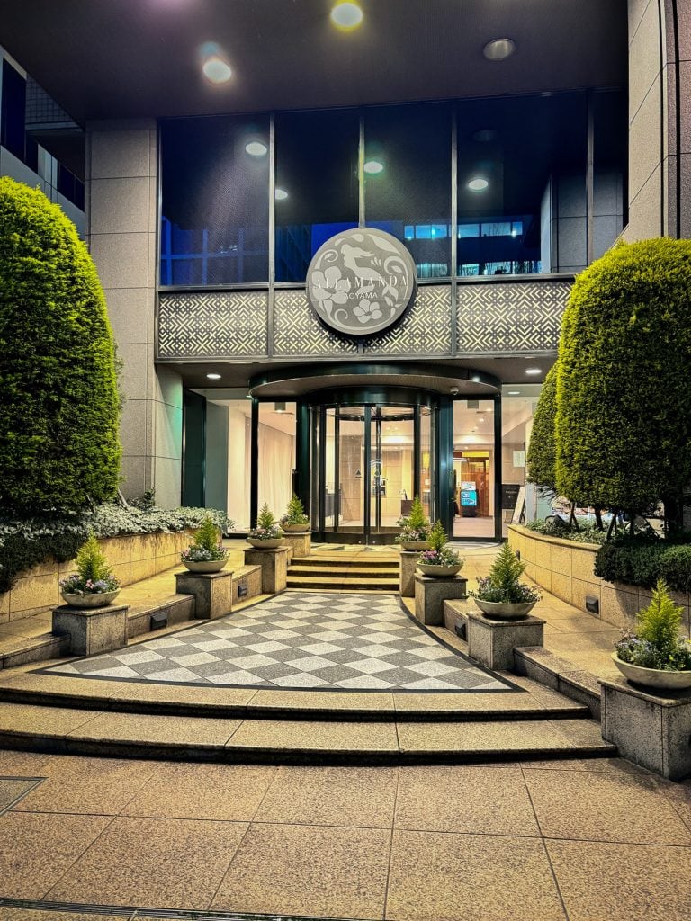 Hotel Allamanda Aoyama Tokyo entrance at night with checkered steps and circular emblem above glass doors