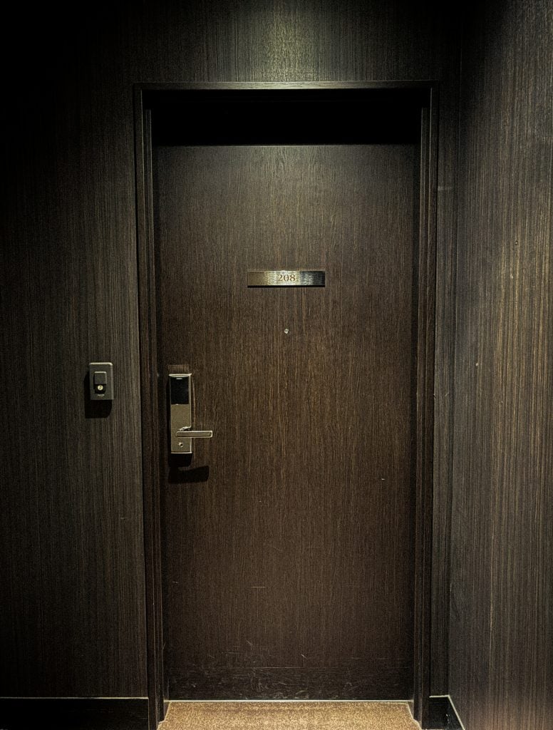Dark wooden hotel door with brushed metal plaque reading “208” at Hotel Allamanda Aoyama Tokyo