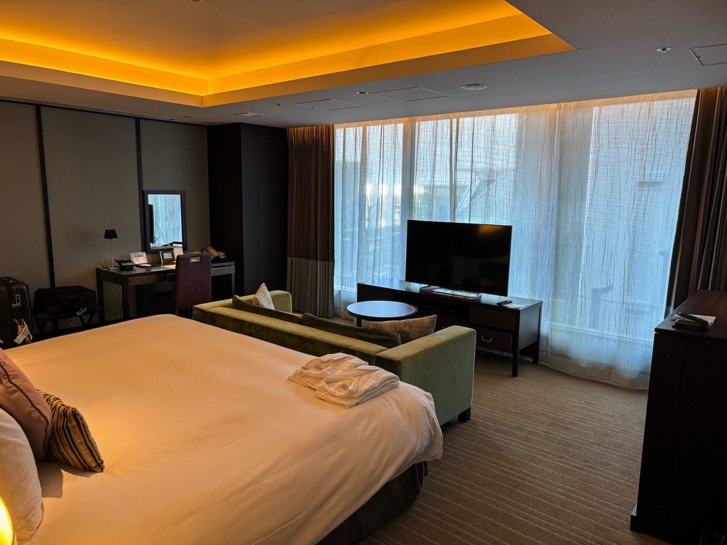 Wide view of Hotel Allamanda Aoyama Tokyo’s Modern Superior Double Room, with wide king bed, velvet sofa, TV, and robes folded on the bed.