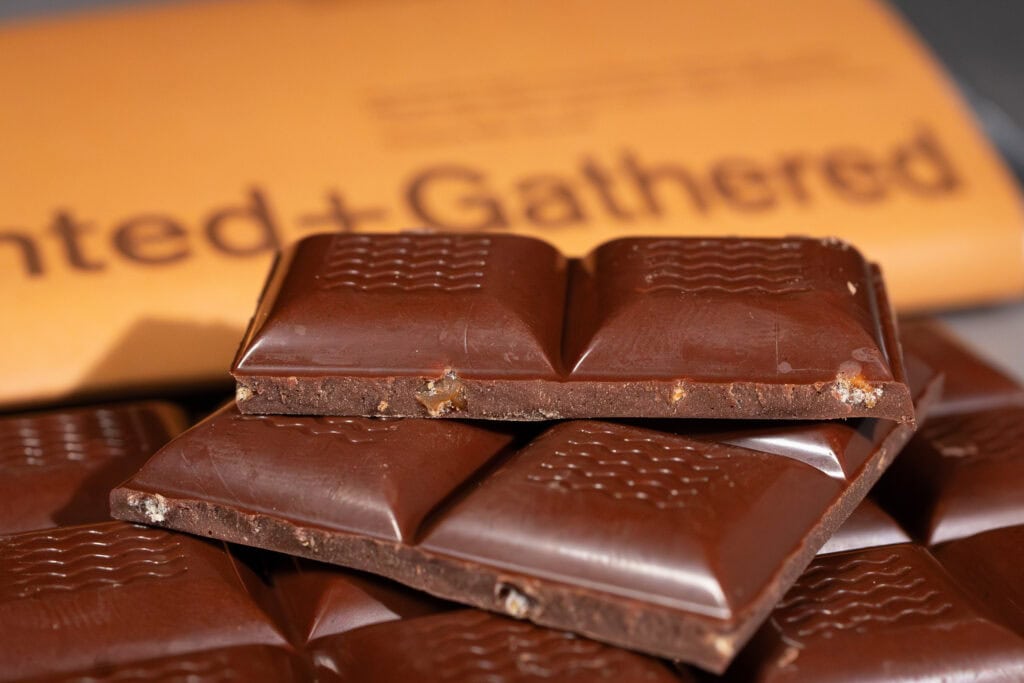 Opened Hunted + Gathered Almond Caramel Milk Chocolate bar showing glossy moulded squares with roasted almond caramel pieces inside.