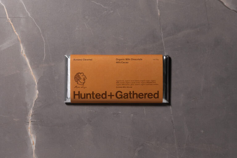 Hunted + Gathered Almond Caramel 46% Cacao Milk Chocolate bar in minimalist brown packaging on grey marble background.