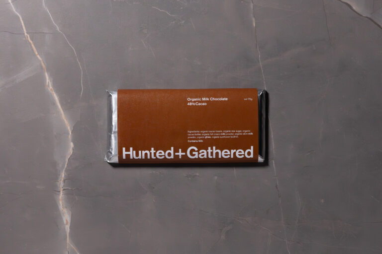 Hunted + Gathered Milk Chocolate 48% bar in brown minimalist wrapper on grey marble background.