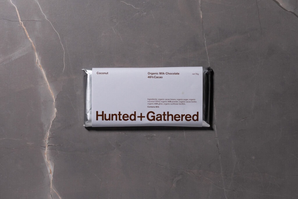 Hunted + Gathered Coconut 46% Cacao chocolate bar in minimalist white packaging on a grey stone background.