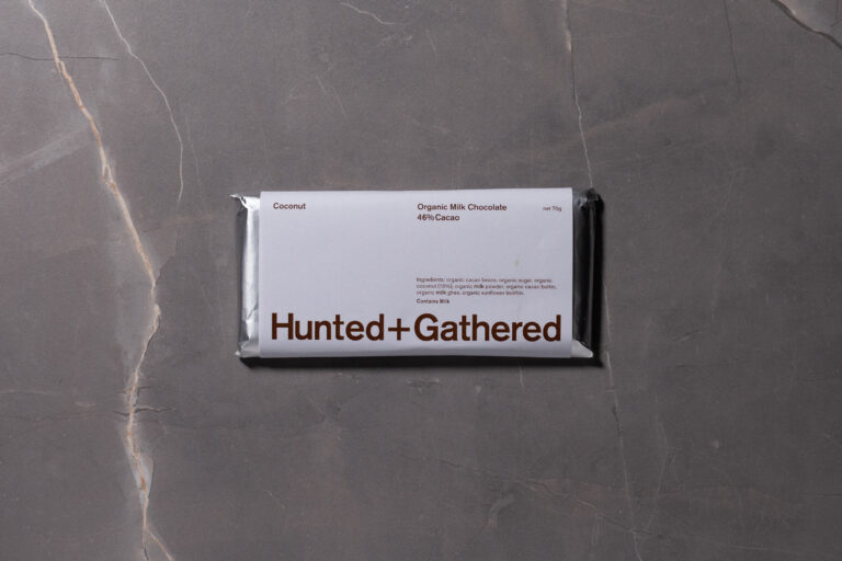 Hunted + Gathered Coconut 46% Cacao chocolate bar in minimalist white packaging on a grey stone background.