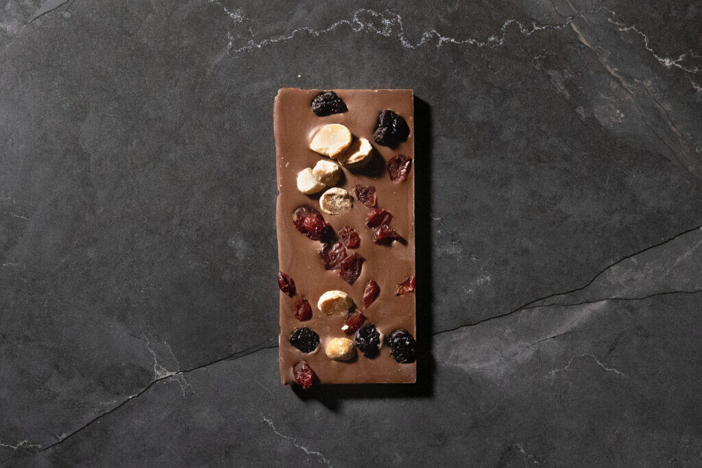 Full Koko Black Cranberry, Macadamia & Cherry milk chocolate bar with visible nuts and fruits on a dark marble background.