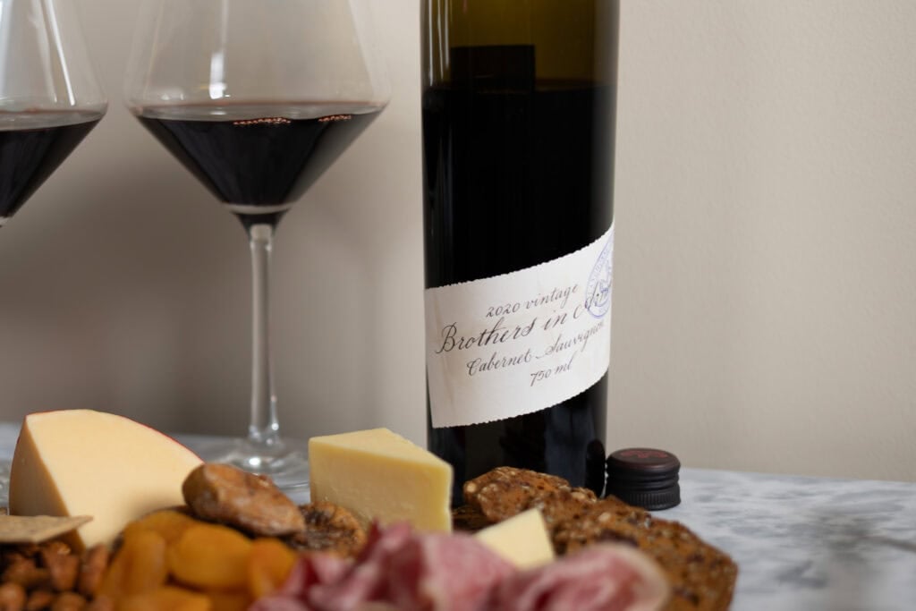 Brothers in Arms Cabernet Sauvignon 2020 with red wine glasses, cheese, crackers, dried fruit, and charcuterie