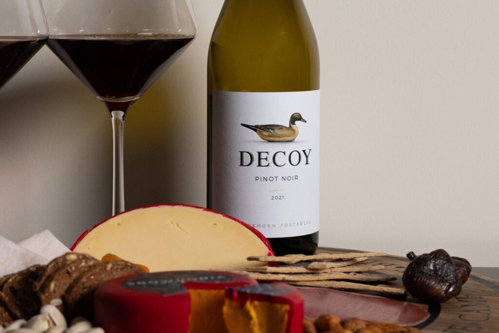 Decoy Pinot Noir 2021 with edam cheese, crackers, turkey, prosciutto, and dried apricots on a tasting board