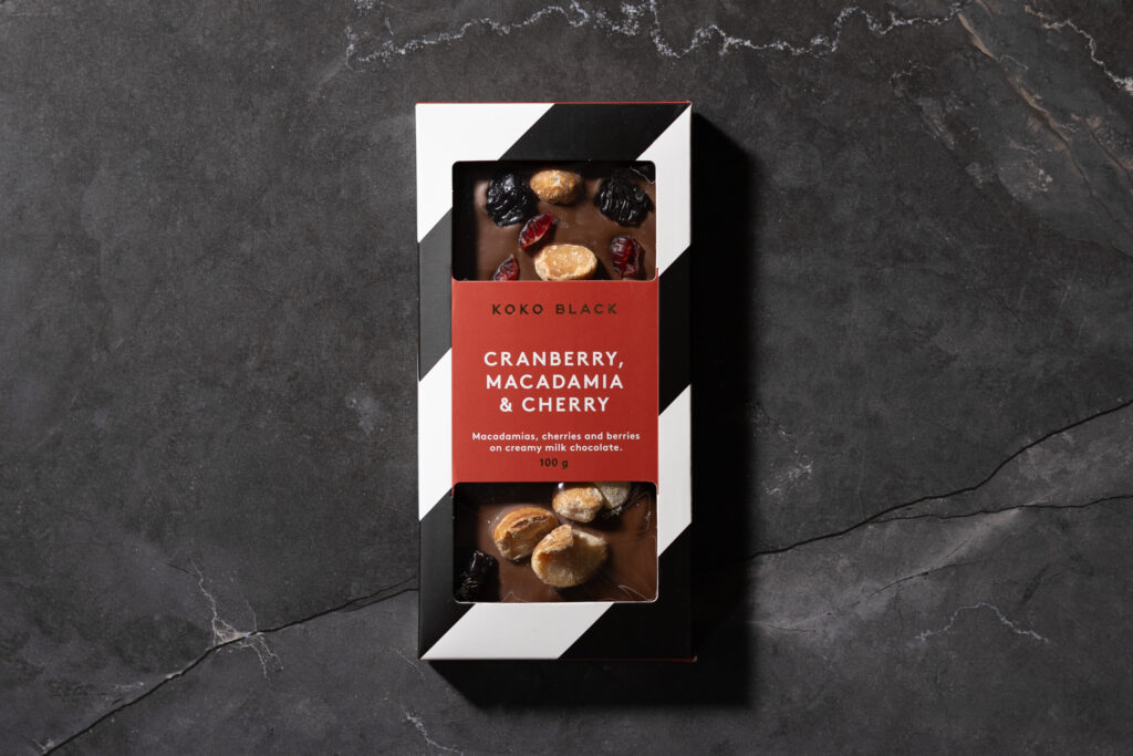 Koko Black Cranberry, Macadamia & Cherry milk chocolate bar in packaging on a dark marble background.