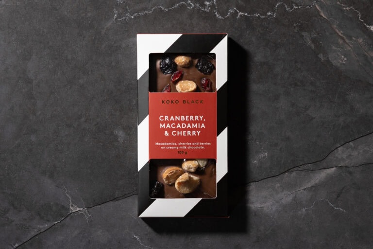 Koko Black Cranberry, Macadamia & Cherry milk chocolate bar in packaging on a dark marble background.