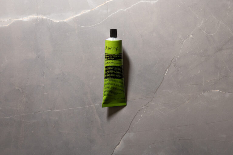 Green tube of Aesop Geranium Leaf Body Balm on a grey stone surface.