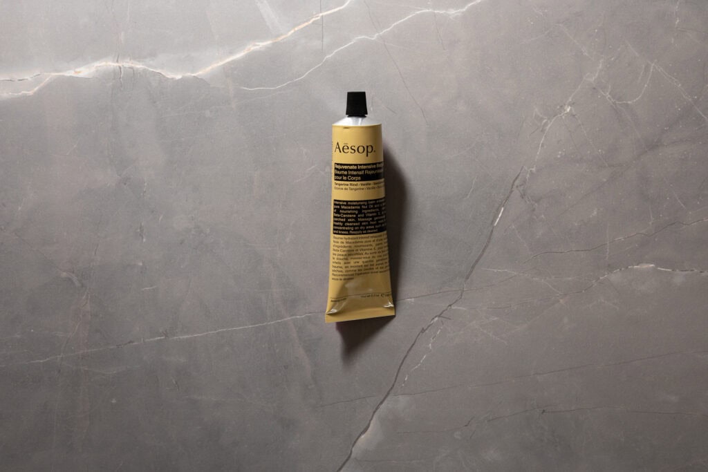 Aesop Rejuvenate Intensive Body Balm tube photographed on a grey stone background