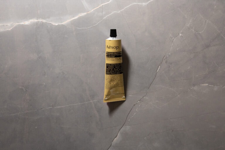 Aesop Rejuvenate Intensive Body Balm tube photographed on a grey stone background