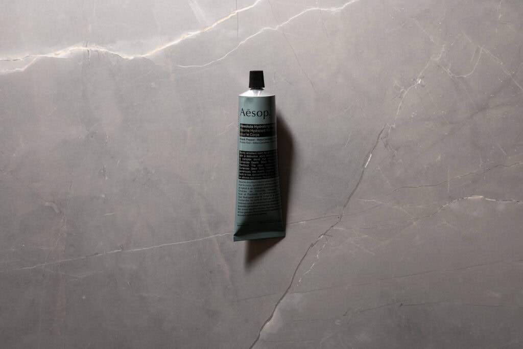 Aesop Resolute Hydrating Body Balm tube photographed on grey stone background