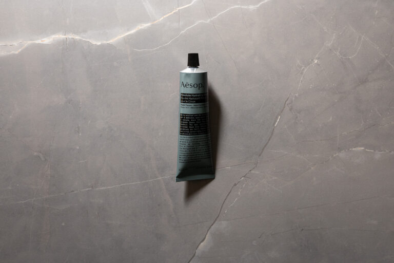 Aesop Resolute Hydrating Body Balm tube photographed on grey stone background