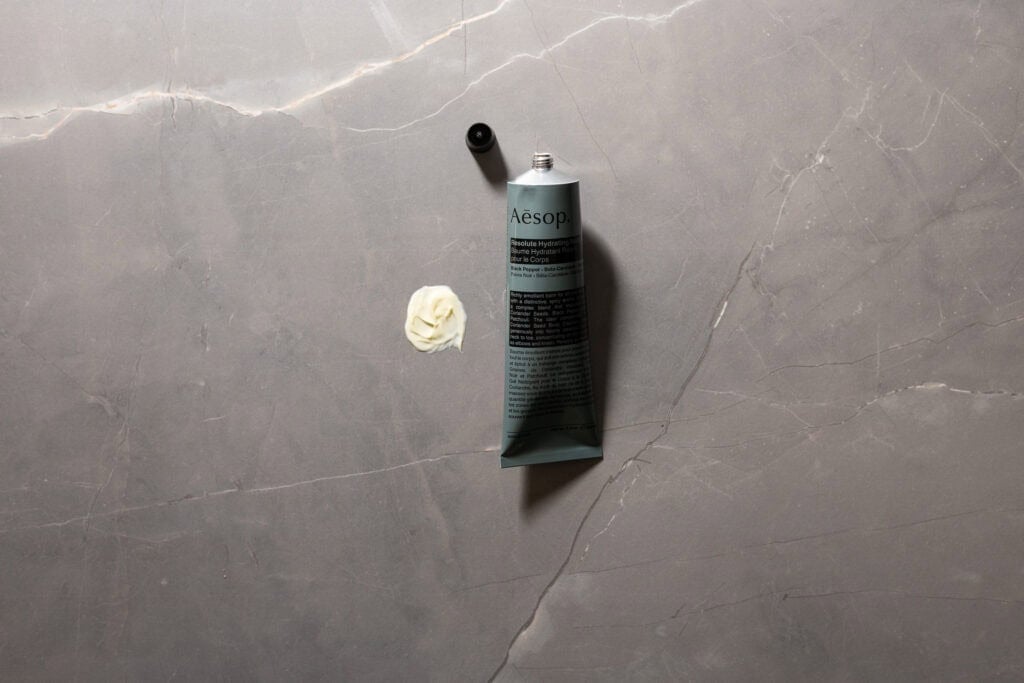 Aesop Resolute Hydrating Body Balm with cream swatch on grey stone background