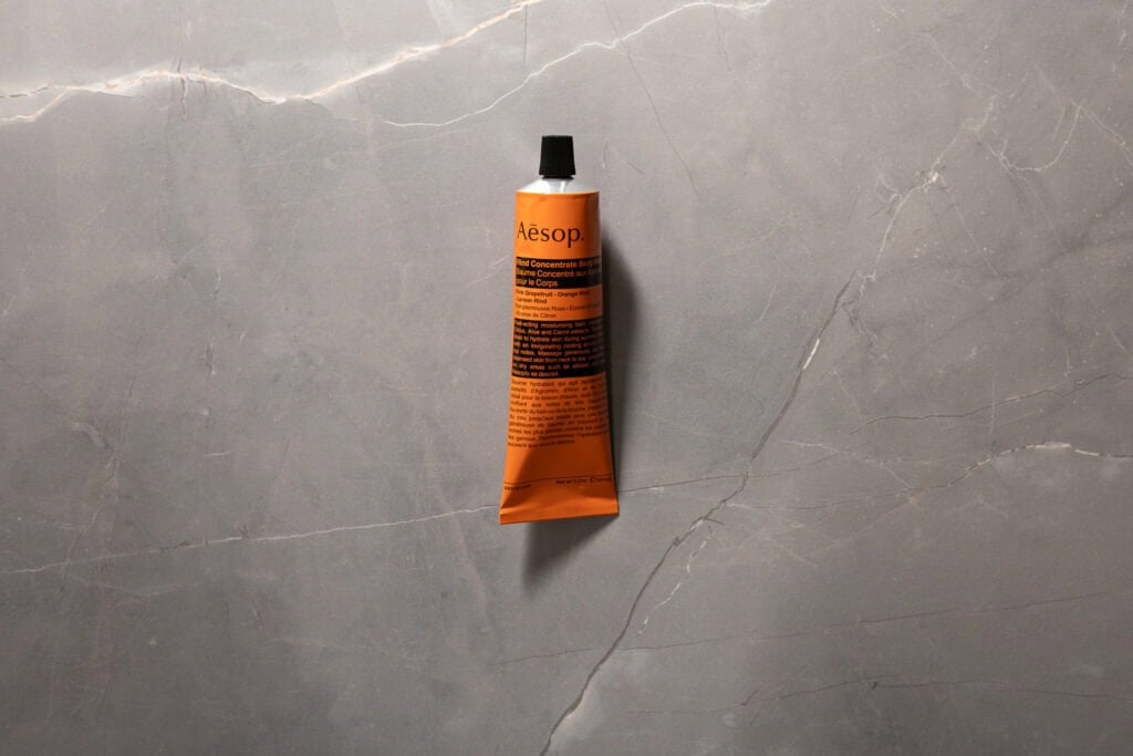 Orange tube of Aesop Rind Concentrate Body Balm against a grey stone background.