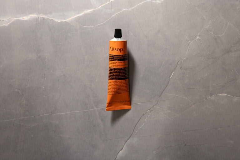 Orange tube of Aesop Rind Concentrate Body Balm against a grey stone background.