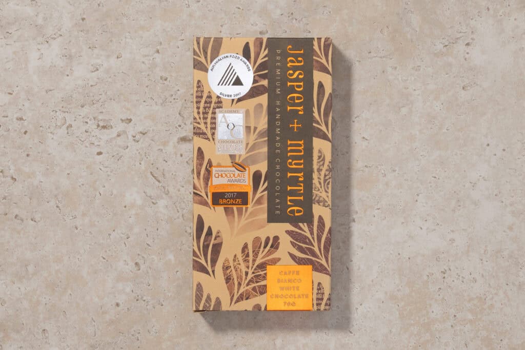 Jasper + Myrtle Caffè Bianco white chocolate bar packaging on a neutral stone surface