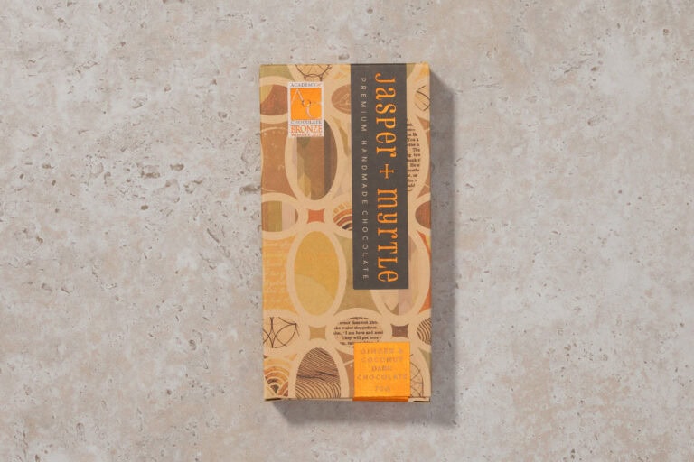 Jasper + Myrtle Ginger & Coconut 65% dark chocolate bar in packaging on a neutral stone surface.