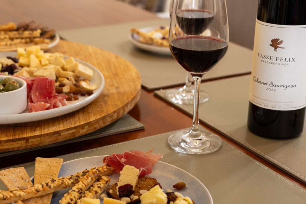 Glass and bottle of Vasse Felix Margaret River Cabernet Sauvignon 2022 beside a cheese and charcuterie tasting board.