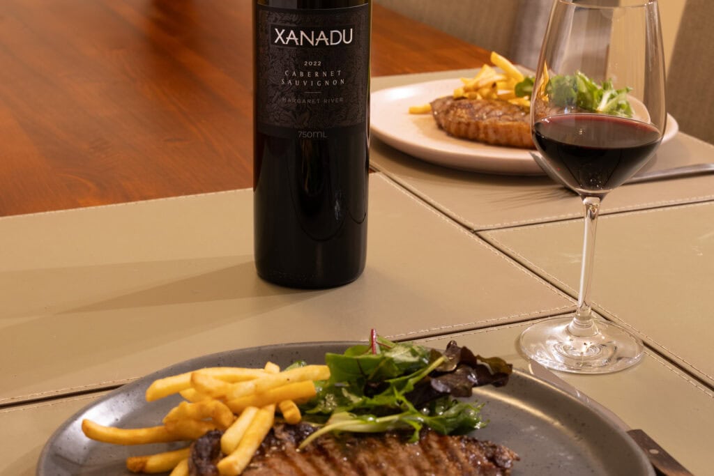 Xanadu Cabernet Sauvignon 2022 with steak, fries and salad on a dining table