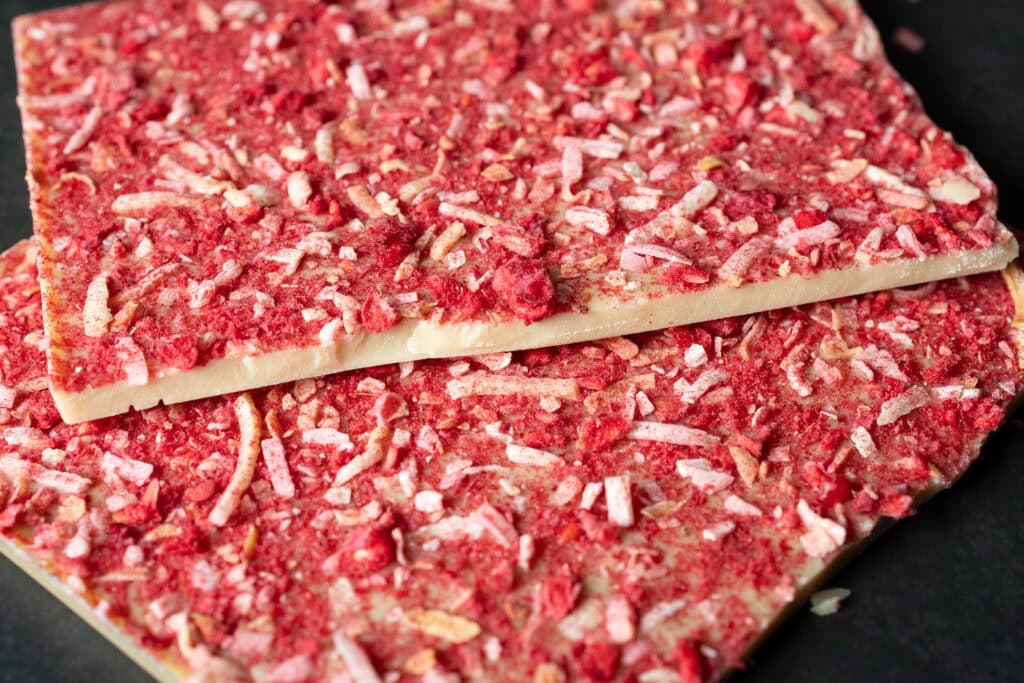 Close-up of Ratio Raspberry & Toasted Coconut White Chocolate showing raspberry pieces, toasted coconut and the thickness of the white chocolate base