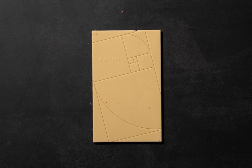 Front side of Ratio Raspberry & Toasted Coconut White Chocolate showing the geometric mould design and smooth white chocolate surface