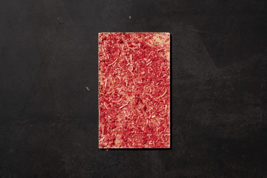 Reverse side of Ratio Raspberry & Toasted Coconut White Chocolate covered with raspberry powder and toasted coconut pieces