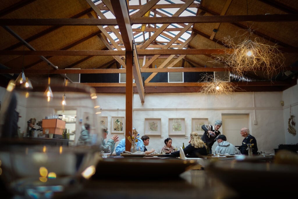 Diners enjoying lunch inside Topiary Restaurant beneath exposed timber beams and skylights.