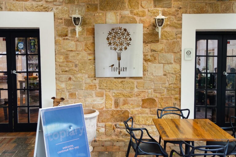 Entrance to Topiary Restaurant featuring a stone façade, outdoor seating and the restaurant’s signature wall sign.