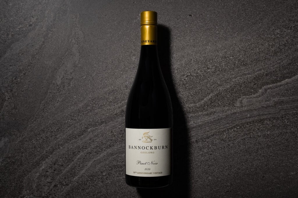 A bottle of Bannockburn Geelong Pinot Noir 2024 standing on a dark grey stone surface, with its cream 50th Anniversary Vintage label and gold capsule visible.