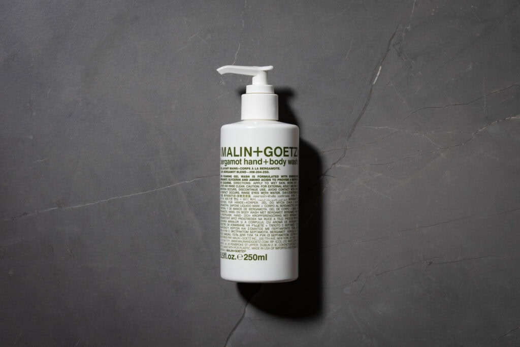 MALIN+GOETZ Bergamot Hand + Body Wash bottle on a dark stone surface