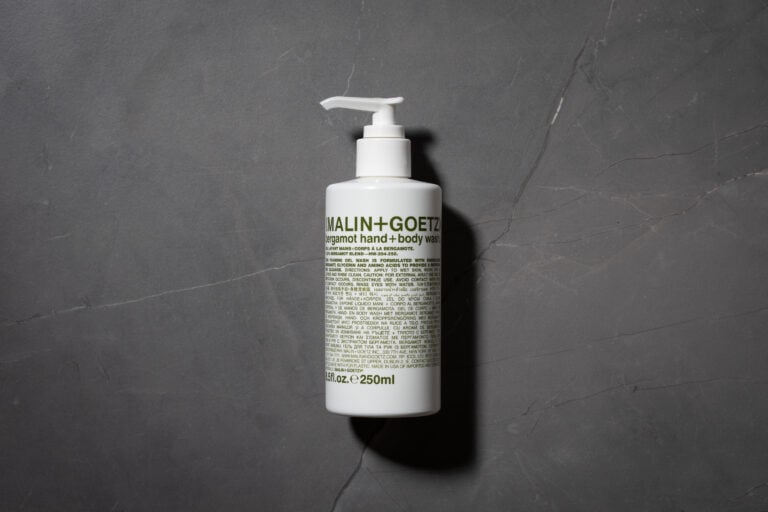 MALIN+GOETZ Bergamot Hand + Body Wash bottle on a dark stone surface