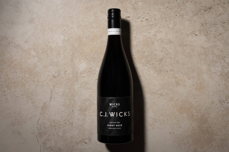 Wicks Estate C.J. Wicks Pinot Noir 2023 bottle standing against a pale stone background, with a black label and long shadow.