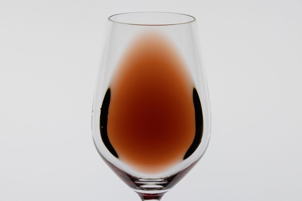 Pale garnet C.J. Wicks Pinot Noir 2023 in a clear wine glass, showing its translucent colour and lighter rim against a white background.