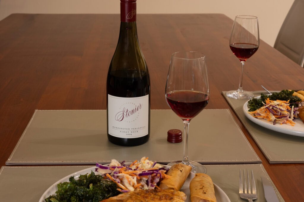 Bottle and two glasses of Stonier Mornington Peninsula Pinot Noir 2024 served with roast chicken, spring rolls, kale and coleslaw.
