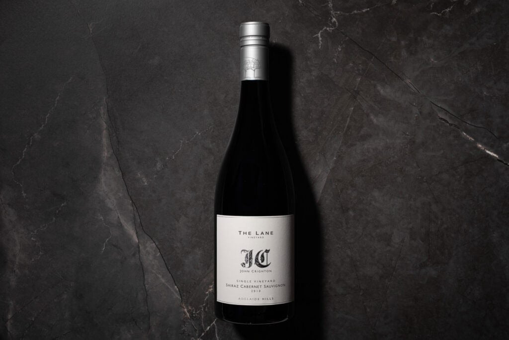 Bottle of The Lane John Crighton Single Vineyard Shiraz Cabernet 2010 on a dark stone background